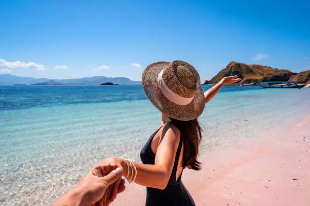Photo of Young couple tourism enjoying the tropical pink sandy beach with clear turquoise water at Komodo islands in Indonesia