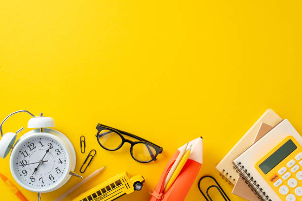 istock Back-to-school scene unfolds from top view, showcasing stationery, notebooks, pencil case, calculator, timer, glasses, car toy, clips. Vibrant yellow backdrop, inviting you to add your text or advert 1547634669
