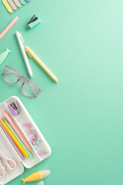 istock Create vibrant back-to-school atmosphere with vertical top view display. Girlish stationery, pencil case, pens, sticky notes, clips, glasses, stapler are arranged on teal backdrop, inviting adverts 1547636454