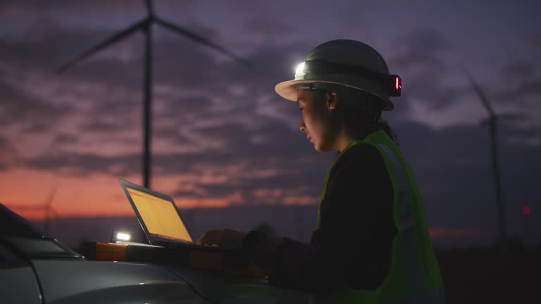 Engineers working with laptop at Wind turbine farm at night