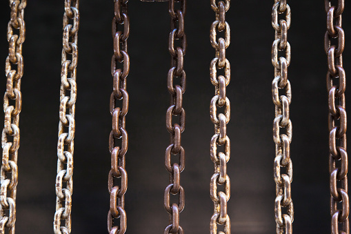 Steel chains directly hang on a dark background close-up.