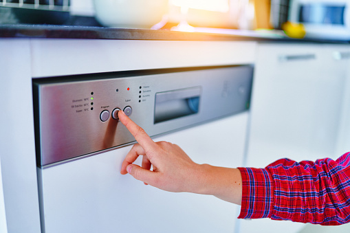 Female finger presses start button of dishwasher