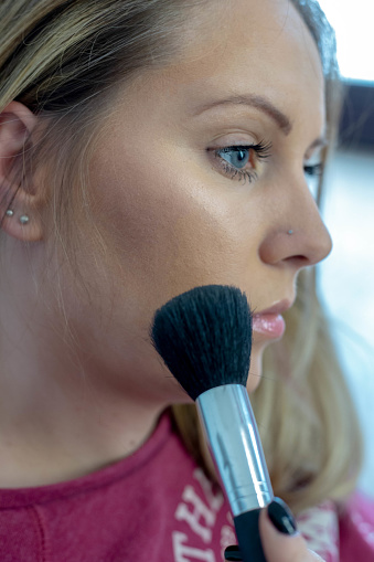 Beautiful young woman applying makeup, closeup
