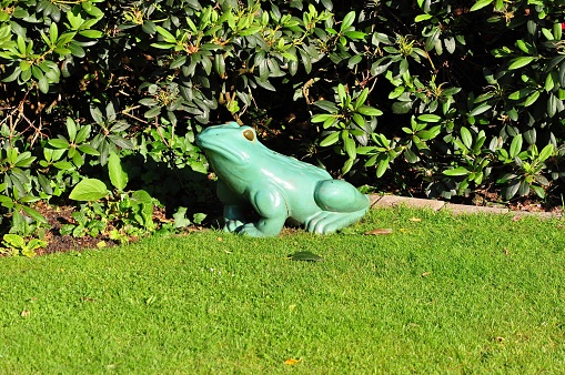 A closeup of a green frog sculpture in a green garden in sunlight