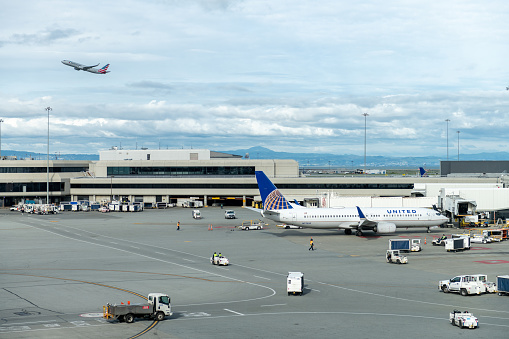 San Francisco, California - April 04, 2019: San Francisco International Airport. United Airlines Boeing is Taxing and Ground Service in Background. American Airlines is Taking Off