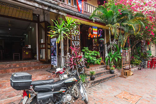 Old streets of Luang Prabang with lush greenery and red chair and tables. Luang Prabang, Laos - March 03, 2023.