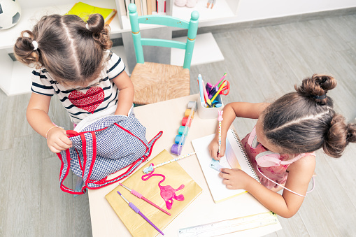 top view, two girls surrounded by school supplies drawing and stuffing things into their school bags.