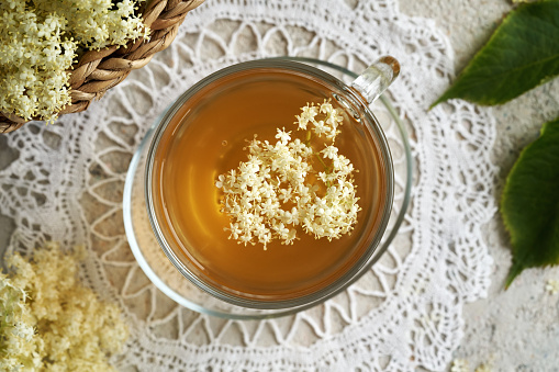 Fresh elderberry flowers in a cup of herbal tea on a table, top view