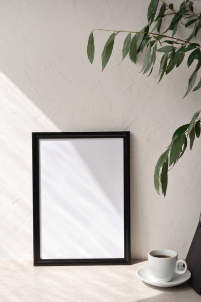 istock Minimalist elegant neutral empty picture frame mockup with geometric sunlight shadow, coffee cup, template for art work poster with copy space. Neutral modern home interior, workspace. Beige background 1547974476