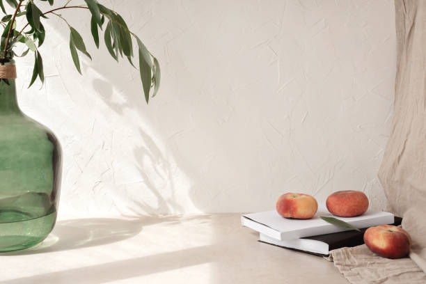 Aesthetic home interior design template, vase with tree branches, peaches, book, glasses on table, empty beige wall background with sunlight shadow