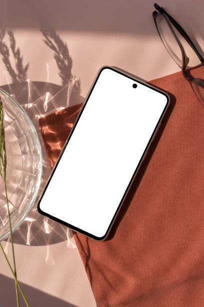 istock Empty mobile phone screen mock up, glasses, aesthetic crystal and floral sun light shadow on terracotta napkin and neutral peach beige background, elegant business branding template 1548012847