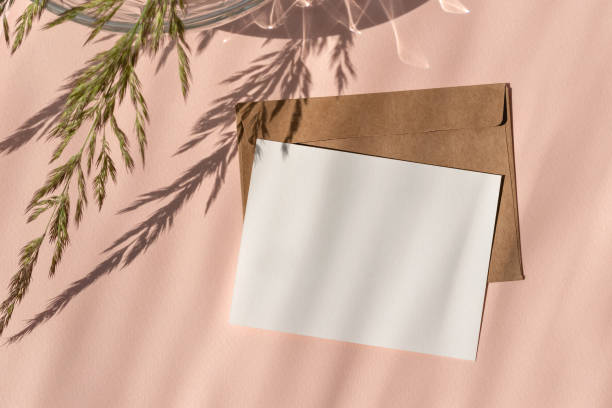 istock Empty paper card mockup, envelope, meadow grass with sunlight shadow on light peach neutral background. Aesthetic wedding invitation, postcard template 1548015485