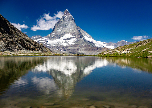 The Materhorn (4478 m a.s.l.) at the Riffelsee, where it is reflected on the water surface. It is one of the highest mountains in the Alps and because of its striking appearance and climbing history, one of the most famous mountains in the world. For Switzerland it is a landmark and in summer days a highly visited natural landscape. Uphill on foot or via rack railroad you can reach the Riffelsee from Zermatt. Photographed in July 2023.