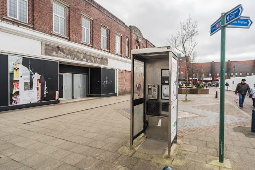 Crewe, Cheshire, England, February 21st 2023. Grimy telephone booth against closed Marks And Spencer store, urban decline editorial illustration.