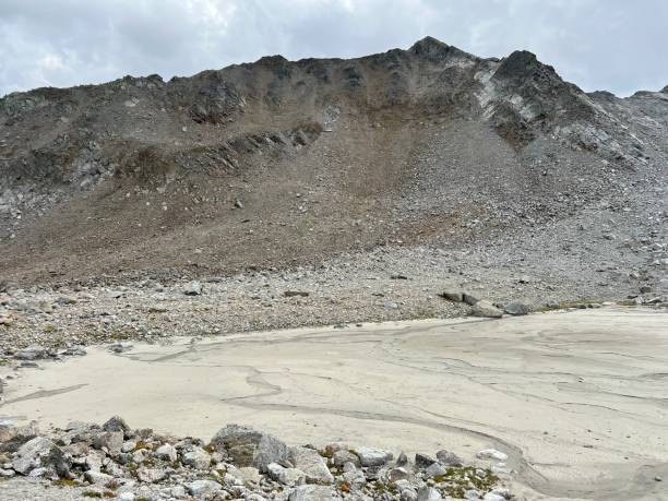 o fundo lamacento de um lago alpino volátil abaixo do cume flüela wisshorn ou fluela wisshorn (3085 m) na cordilheira dos alpes silvretta, davos - cantão de grisons, suíça (kanton graubünden, schweiz) - global warming drought riverbank dirt - fotografias e filmes do acervo