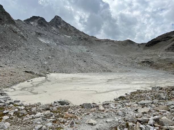 o fundo lamacento de um lago alpino volátil abaixo do cume flüela wisshorn ou fluela wisshorn (3085 m) na cordilheira dos alpes silvretta, davos - cantão de grisons, suíça (kanton graubünden, schweiz) - global warming drought riverbank dirt - fotografias e filmes do acervo