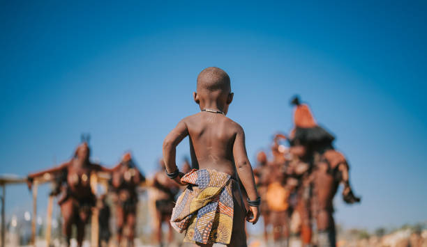 rear view Namibian Himba child looking at villagers rear view Namibian Himba child looking at villagers kaokoveld stock pictures, royalty-free photos & images