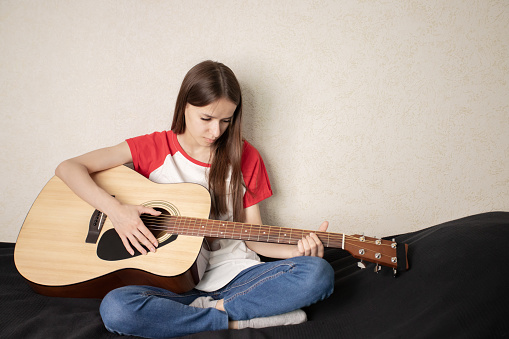 teenager girl playing guitar at home in teen room, girl learning to play the guitar as a hobby