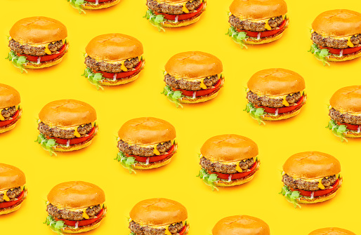 Side view from above of seamless pattern of tasty fresh juicy homemade real lots of hamburgers with beef patties, cheddar cheese, tomato, onion and salad isolated on a yellow background with shadow