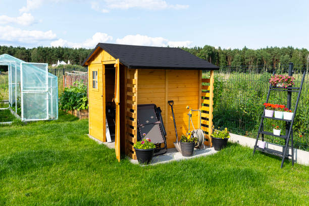 a wooden garden shed standing on a concrete foundation in a garden, flowers and tools visible. - shed imagens e fotografias de stock