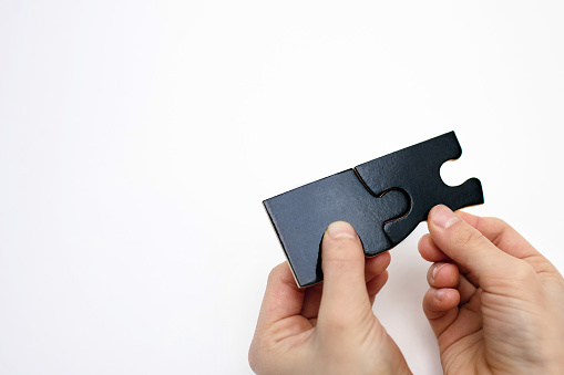 Two connected black puzzles in the hands of a child on a white background close-up. Puzzle for the development of children's intelligence. Connection concept with free space for text