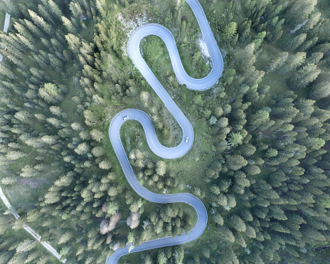 Atmospheric mountain road through the forest with serpentine hairpin bends photographed from above by drone in the heart of the Dolomites