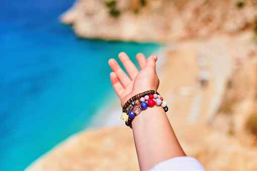 Hand of traveler girl with bracelets leading to the sea at sunny day