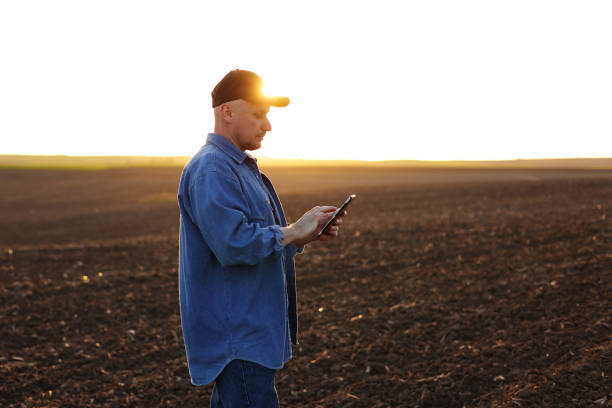 istock Smart farming technology and agriculture. Farmer uses digital tablet on field with plowed soil at sunset. Checking and control of soil quality, land readiness for sowing crops and planting vegetables 1548272191