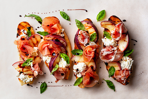 Food background with open sandwiches. Toastet bread, griddled peach, parma ham or prosciuto and robiola cheese, with balsamic vinegar and basil. Directly above.