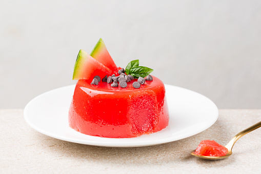 A jellied watermelon pudding, made with watermelon pulp, sugar and starch, decorated with chocolate, fresh fruit and basil leaves. Sicilian summer dessert gelo di melone. White background.