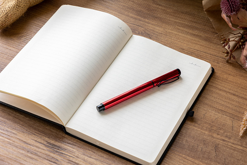 Red pen on open cover notebook with blank pages on wooden table