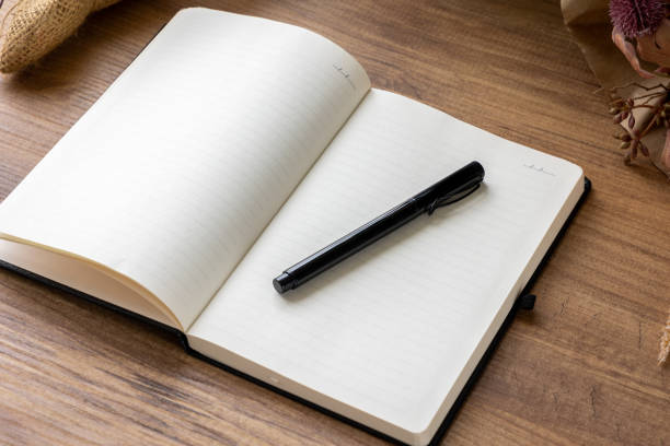 istock Black pen on open cover notebook with blank pages on wooden table 1548295860