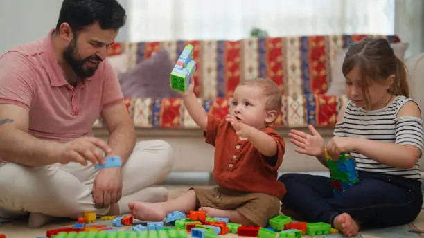 Photo of Father playing and entertaining his small baby boy and his daughter in living room at home