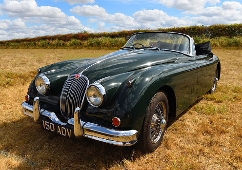 Little Gransden, Cambridgeshire, England - August 28, 2022: Classic 1960 Jaguar XK150 drop head coupe parked in field.