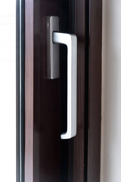 istock Aluminum silver handle on close door, window against brown frame background. Close up view. Vertical 1548356370