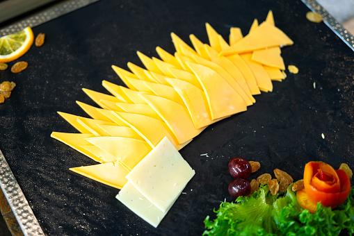 Sliced pieces of cheddar cheese which aligment on black ceramic plate. Food object photo, close-up and selective focus.