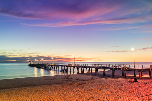 Henley Beach jetty at dusk with the tranquil sea embracing the weathered pillars with purple clouds above, South Australia