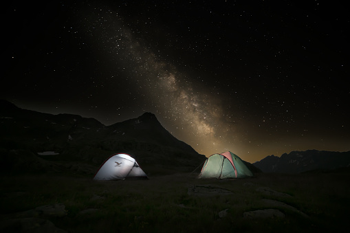 Two illuminated tents on a meadow at an altitude of 2,700 metres on the Gavia Pass. Starry night sky with the milky way. Scene without people immersed in the mountainous nature of the Stelvio National Park