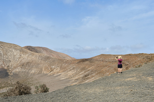 Woman with a backpack, hiking on the Caldera Blanca volcano in Lanzarote and taking pictures amazed by the landscape.