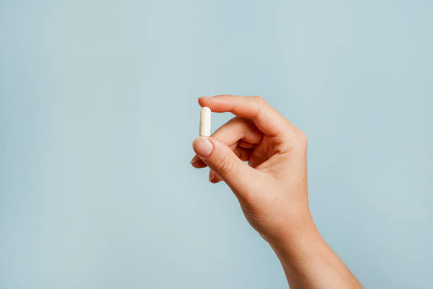 pillola bianca in mano femminile su sfondo blu, prendendo il farmaco - dose capsule vitamin pill pill foto e immagini stock