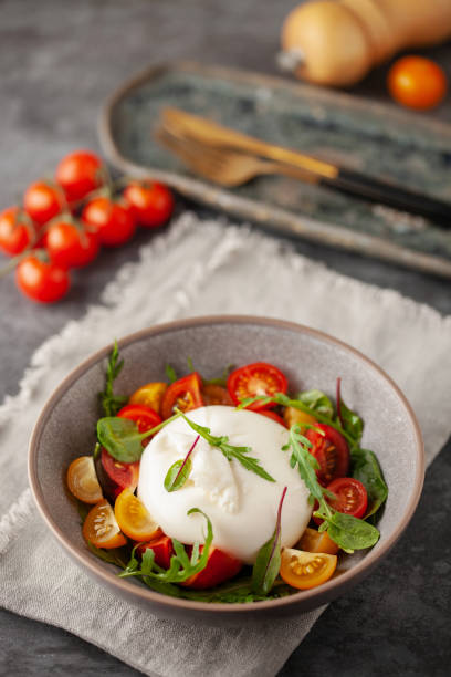 salat mit traditionellem italienischem buratta-käse mit kirschtomaten und rucolablättern in schüssel auf dem tisch - cherry tomato fotos stock-fotos und bilder