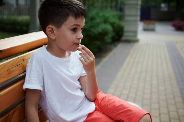 istock Adorable Caucasian elementary age school boy snacking outdoors, sitting on a wooden bench in the city park on summer day 1548598063