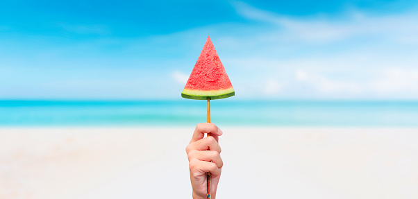 men hand with piece of juicy watermelon on summer beach background