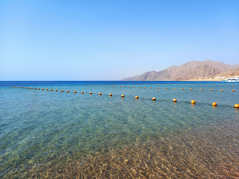 Line of yellow buoys floating in the water of the Red Sea. Panoramic view of Dahab coastline in the Egyptian desert. Beaconing and aquatic signage.