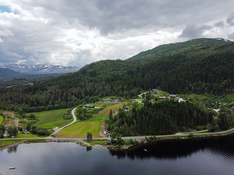 Aerial view, drone shot of Norwegian fjord mountains with green pines and private houses.