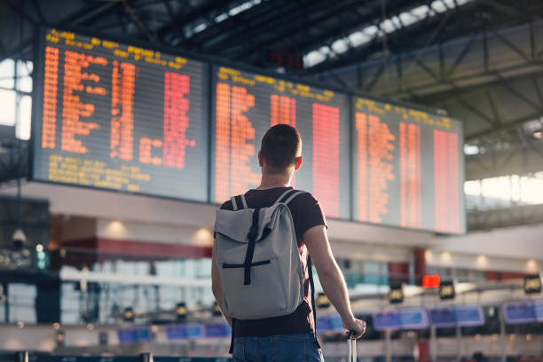 Man walking with backpack and suitcase walking through airport terminal Traveling by airplane. Man walking with backpack and suitcase walking through airport terminal and looking at departure information. airport stock pictures, royalty-free photos & images