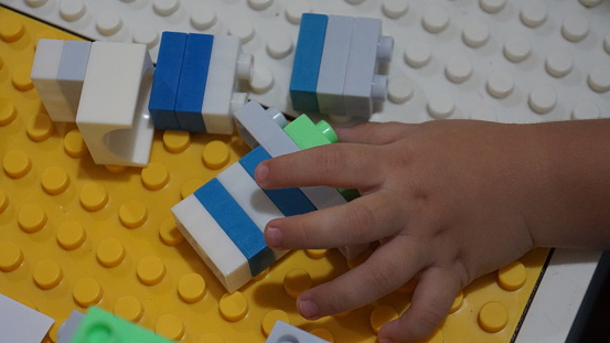 Close up of child's hands playing with colorful plastic bricks blocks at the table.