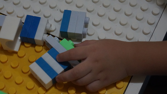 Close up of child's hands playing with colorful plastic bricks blocks at the table.