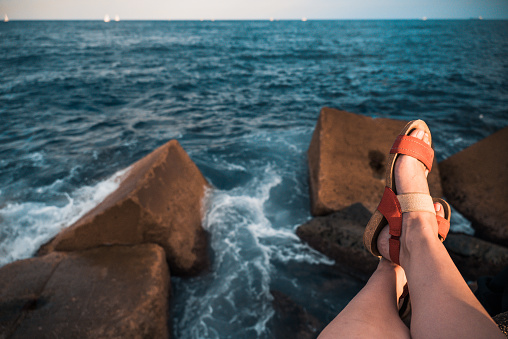 Close-Up Of Female Legs In Red Sandals On Blurred Background Of Breakwaters And Sea With White Yachts. The Concept Of Relaxation And Enjoyment Of Life.