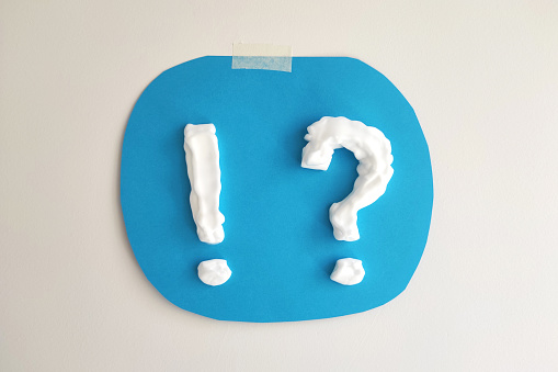 Question mark and exclamation mark made of cream or shaving foam on blue background